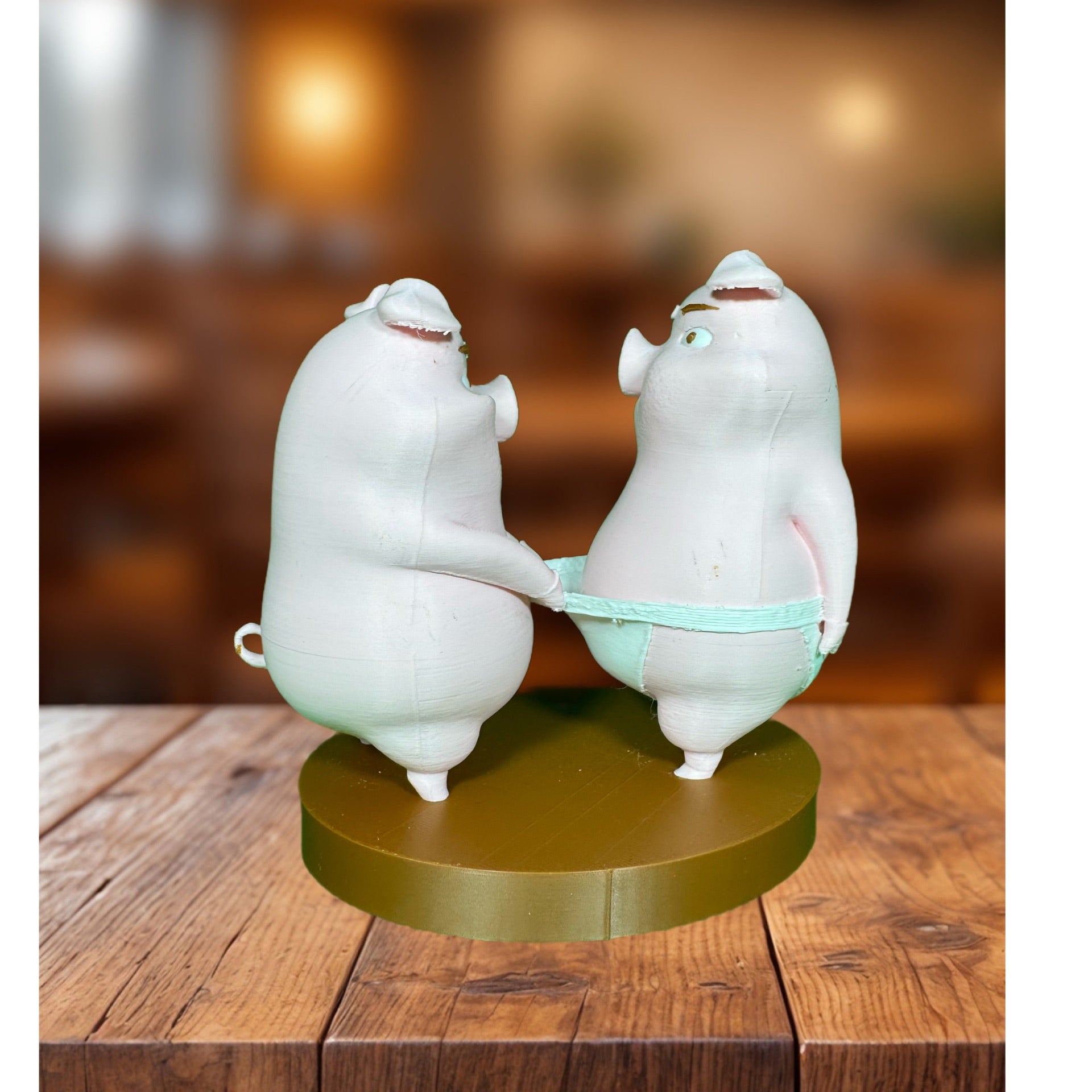 Front view of two 3D printed pig figurines on a gold circular base, sharing a mint-green object